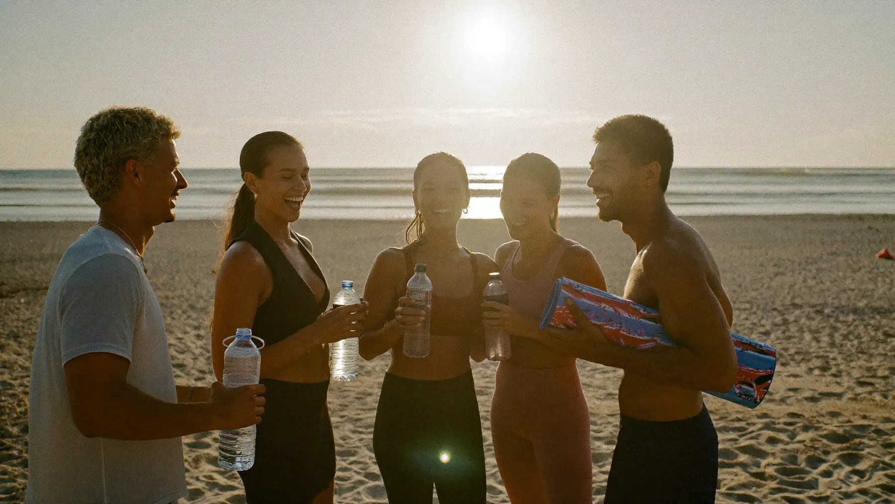 A group of friends laughing together after an outdoor beach workout at golden hour