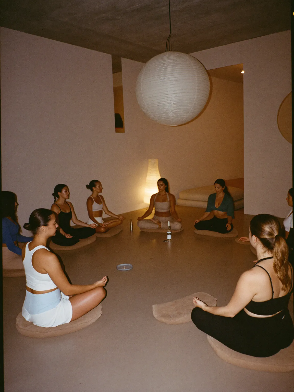 A guided breathwork circle seated on cushions in a warm, minimal interior