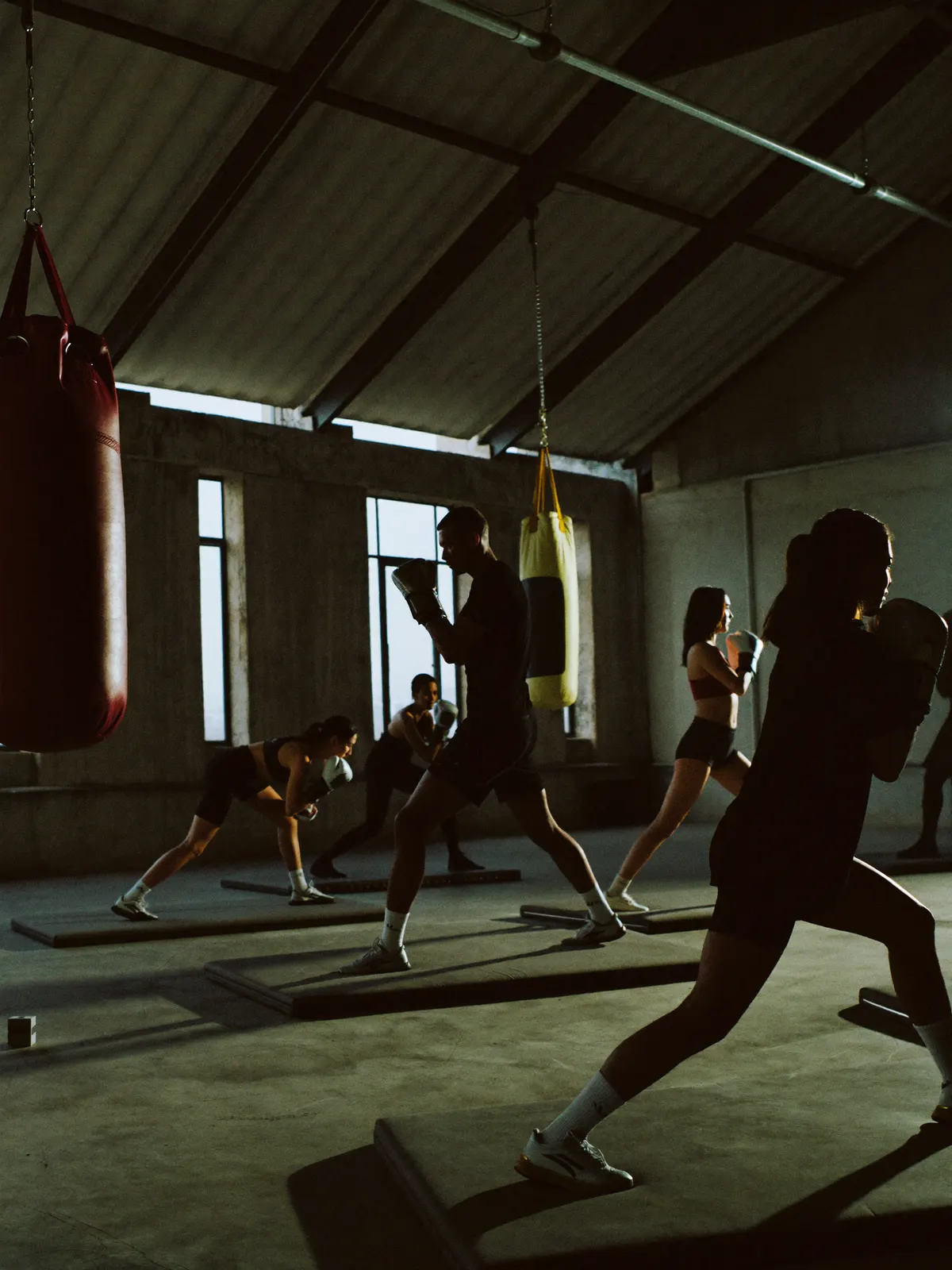A boxing conditioning class working pads in a moody industrial warehouse