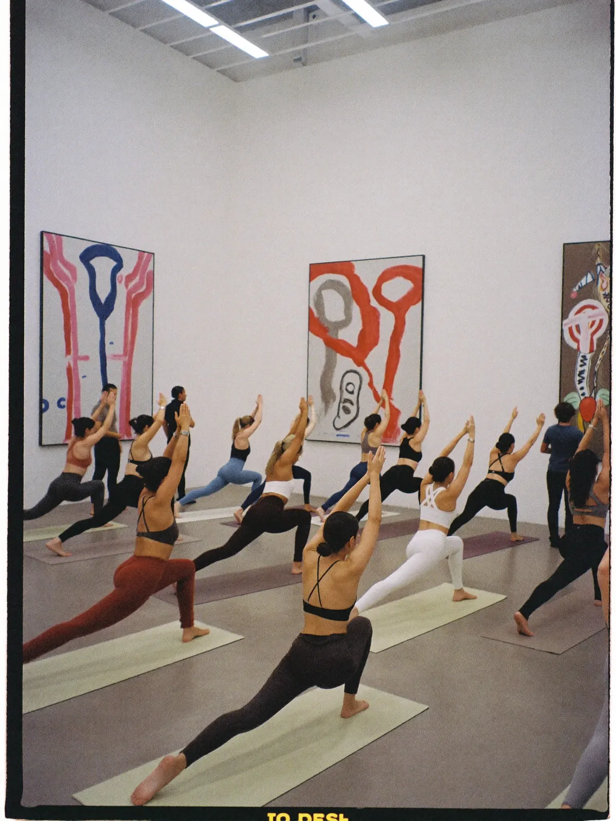 A yoga class holding warrior pose inside a bright contemporary art gallery