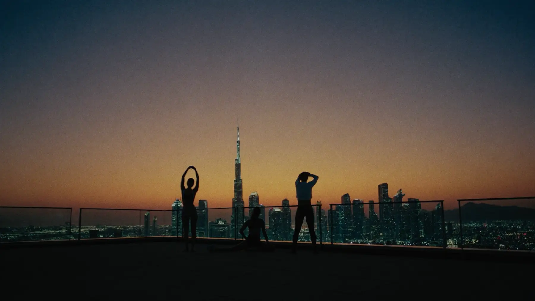 Silhouettes stretching on a rooftop at dusk against the Dubai skyline