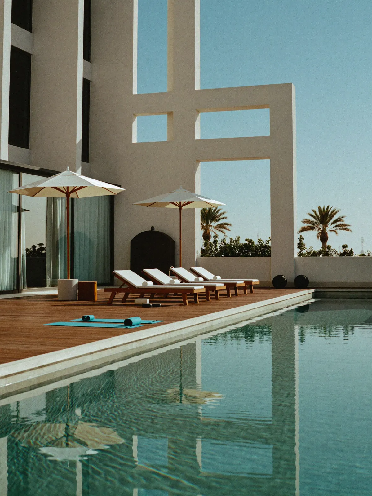 A pristine hotel pool deck in crisp morning light with mats on the decking