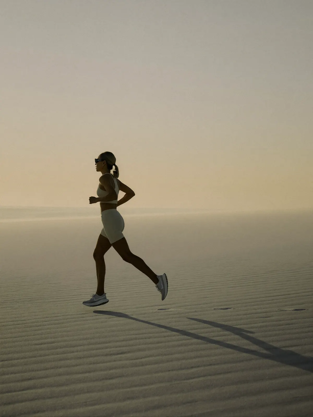 A lone runner on an empty pale beach at hazy sunrise under a vast soft sky